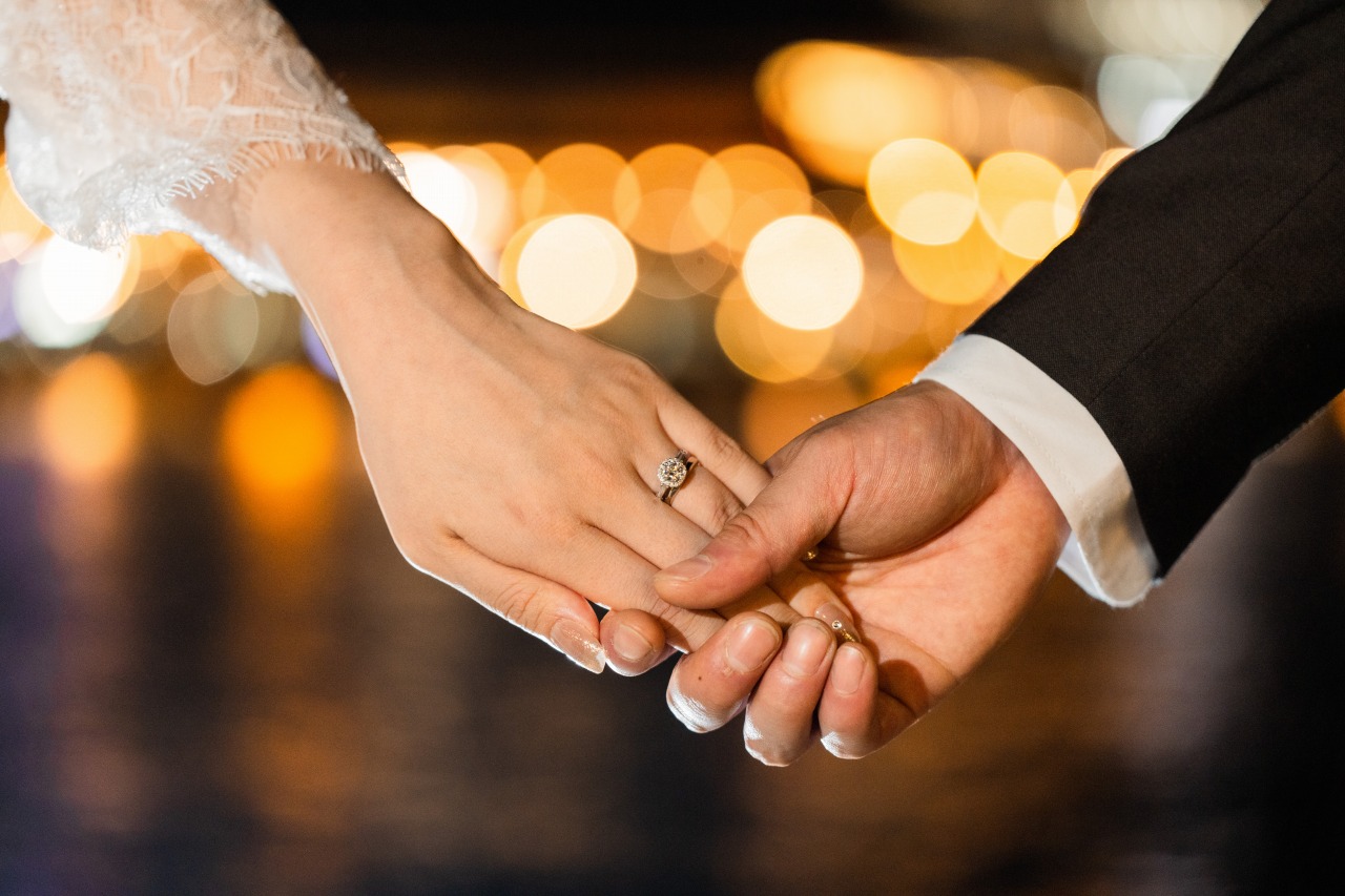 Close-up photo of a couple holding hands with rings at night