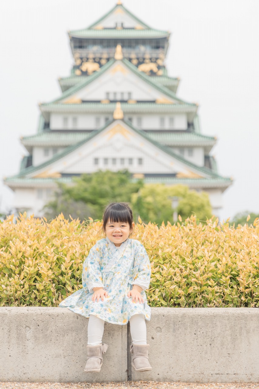 Osaka Castle Park family photoshoot – child sitting foreground with Osaka Castle bokeh backdrop