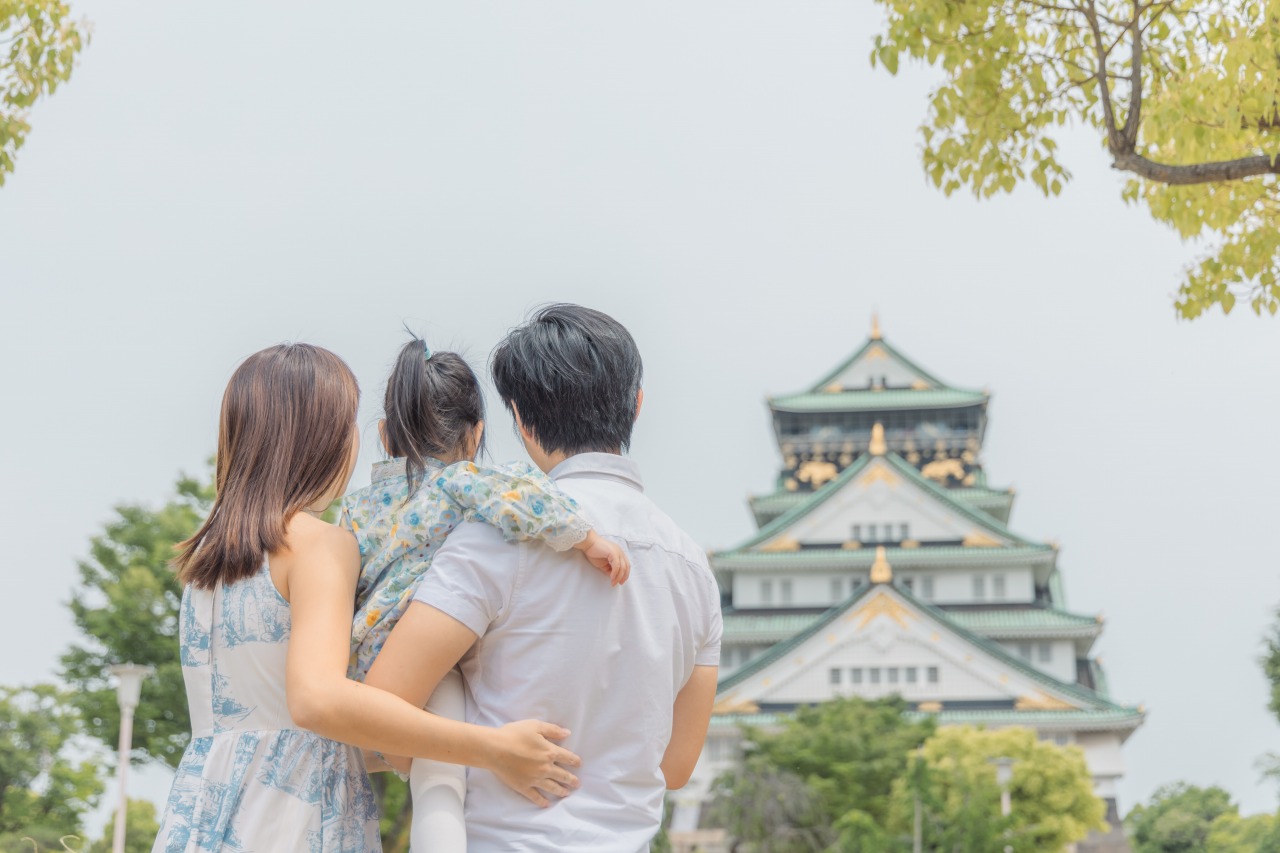 Osaka Castle Park family portrait – parents holding child, castle view