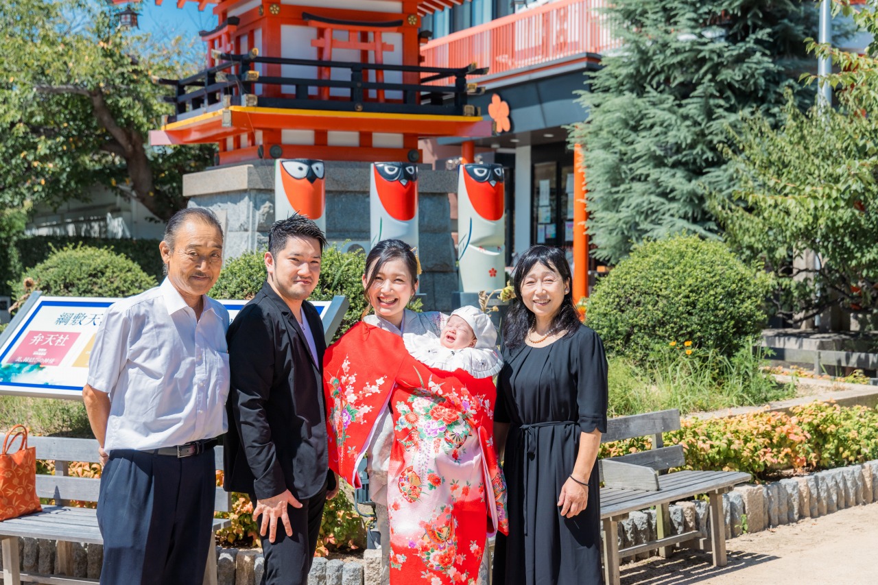 綱敷天満宮 お宮参り 本殿前で家族集合写真 朱色の社殿と緑の庭