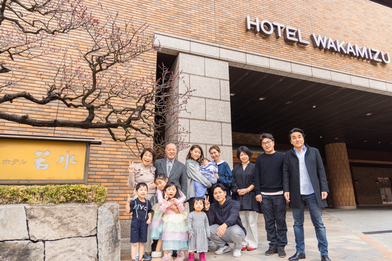 長寿祝い 家族集合写真 ホテル外観前で三世代の記念撮影